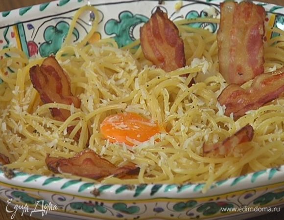 Спагетти еще немного поперчить, выложить на макароны сверху желтки пашот, посыпать оставшимся сыром и украсить чипсами из бекона.
