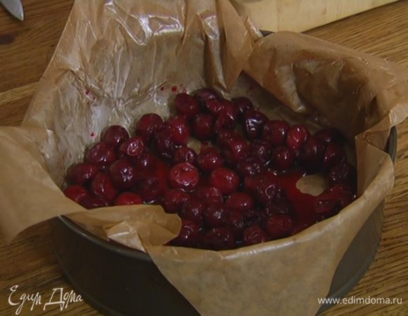 Разъемную форму для выпечки выстелить пищевой бумагой, смазанной оставшимся сливочным маслом, и выложить на дно размороженную вишню вместе с выделившимся соком.