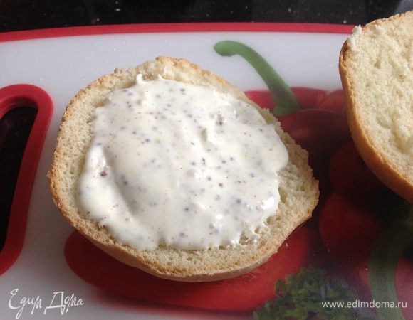 Булочку для гамбургера разрежьте вдоль, нижнюю часть булки обильно смажьте соусом.