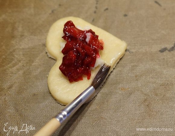 На противень, застеленный пергаментом выложить заготовки теста-сердечки, сверху выложить сливочный сыр и вишневую начинку. Белок слегка взбить с молоком. Маленькой кисточкой смазать им края пирожков. Лучше смазывать по 2-3 пирожка за один раз, чтобы белок не подсыхал и тесто потом лучше склеилось.