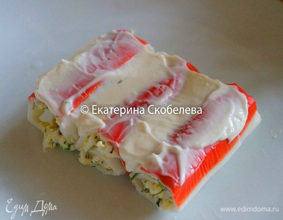 Свернуть палочки в рулет. Выложить поэтапно на блюдо. Первый слой промазать майонезом. Сверху снова положить палочки. Салат должен получиться похожим на крышу дома.
Готовый салат смазать сверху майонезом и посыпать натертым сыром. Приятного аппетита!