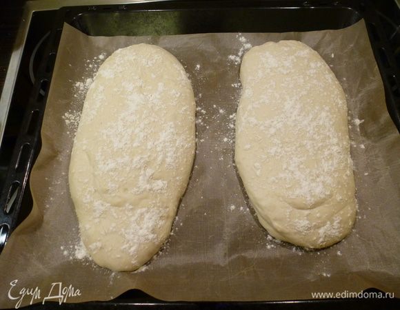 Чтобы тесто не прилипало, смазываем руки маслом. Делим тесто на 2 части и выкладываем на противень. Присыпаем сверху мукой и оставляем еще на 40 минут для расстойки, прикрыв полотенцем.