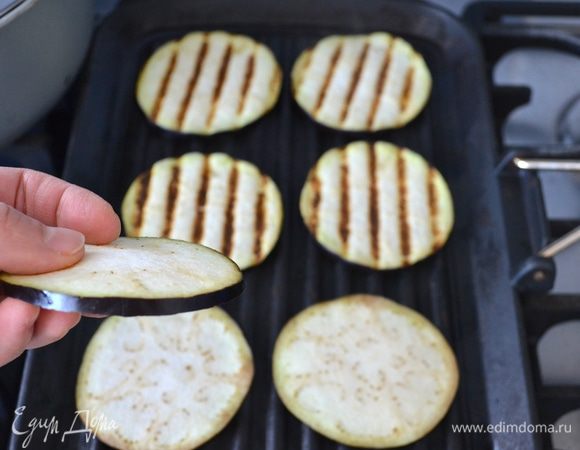 Первым делом баклажан вымыть и тонко нарезать кружочками. Обжарить на хорошо разогретой сковороде-гриль с двух сторон без добавления масла. Сложить на тарелку и ненадолго отставить.