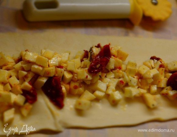 Слоеное тесто разморозить и раскатать в длинный прямоугольник. Уложить начинку, немного отступив от краев. Поднять края и защипить.