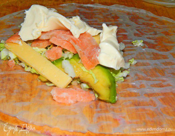 Быстро намочить лист рисовой бумаги под холодной водой с обоих сторон. Долго не держать под водой, иначе он у вас превратится в тряпочку и склеится. Положить на досочку. Выложить на край 2 ст.л. салата, 2 ст.л. сыра филадельфия, 2 полоски семги, 2 тонкие дольки авокадо, полоску сыра. Сложить с коротких сторон вовнутрь и свернуть ролл.