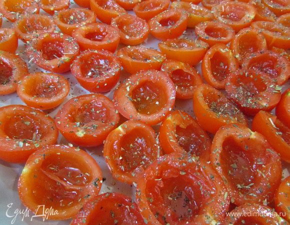 Затем выложить половинки помидоров на противень, застеленный пекарской бумагой (у меня тефлоновый коврик). Сбрызнуть оливковым маслом (2 ст.л.) и присыпать базиликом.