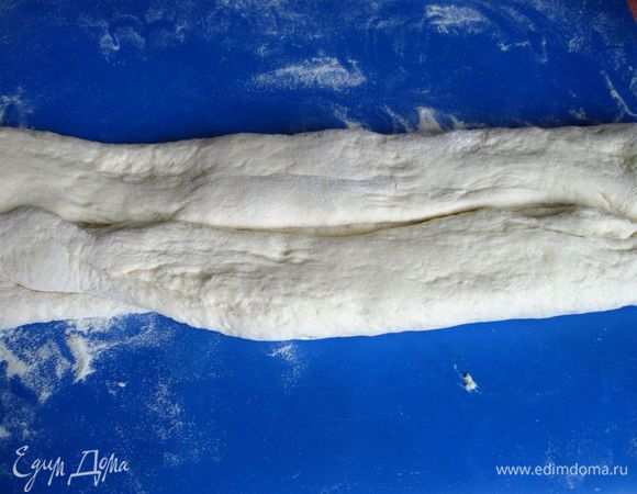 Завернуть крaя теста с двух, более длинных, сторон по направлению к центральной линии.Слегка потянуть, взявшись за концы  заготовки из теста, чтобы получился продолговатый кусок теста длиной около 30 см. 