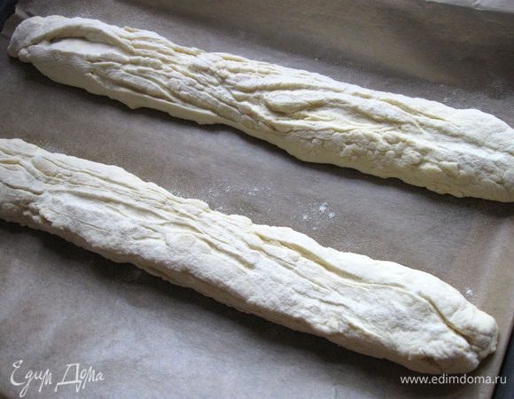 Духовку разогреть до 250С вместе с дополнительным противнем, в который будете наливать воду, когда поставите хлеб. 
Перевернуть тесто и перенести на лист бумаги для выпечки на противень, одновременно растягивая   до максимально возможной длины (длина противня). Чуть присыпать мукой.