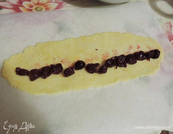 Из каждой части раскатать прямоугольник приблизительно 25*10 см. Это удобно делать на бумаге для выпечки, накрыв тесто вторым листом бумаги.
По длинному краю выложить ряд вишенок.