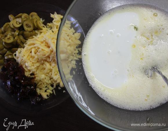 Поставить духовку разогреваться до 180 градусов. 
Сыр натереть на крупной терке, оливки нарезать кружочками, помидорки измельчить.
Соединить в миске кукурузную муку и разрыхлитель. Можно посолить, учитывая соленость добавок.
В отдельной посуде взбить яйца, добавить к ним кефир и масло. 
Соединить обе смеси. Тщательно перемешать.