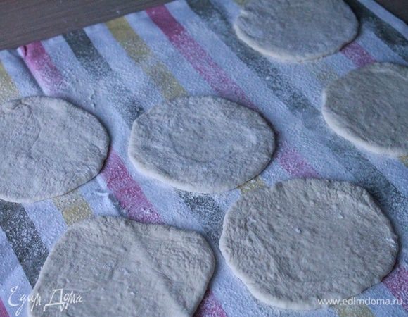 Каждую булочку раскатать в лепешку, положить на пекарскую бумагу и прикрыть полотенцем. Оставить на 15 минут.