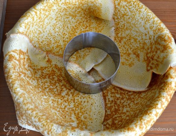 На дно формы (диаметром 26 см) положить пекарскую бумагу. Выложить оставшиеся 4 блина таким образом, чтобы они закрыли всю площадь и их края свисали за бортики формы. В центре при помощи формочки с острыми краями вырезать круг.