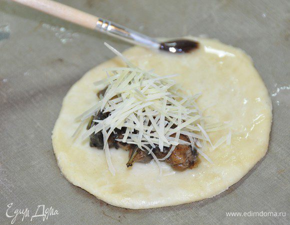 На половину каждого круга (ближе к краю) выложить подготовленную начинку, сверху присыпать натертым на мелкой тёрке пармезаном. Смазать край взбитым яйцом. 