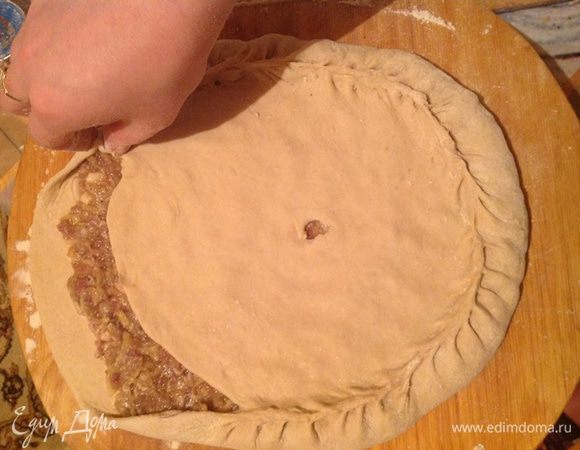 Выкладываем верхний слой теста, то есть маленький. Поднимаем нижнюю часть к верхней и зажимаем края. Делаем в центре дырочку, чтобы оно не набухлось при запекании.