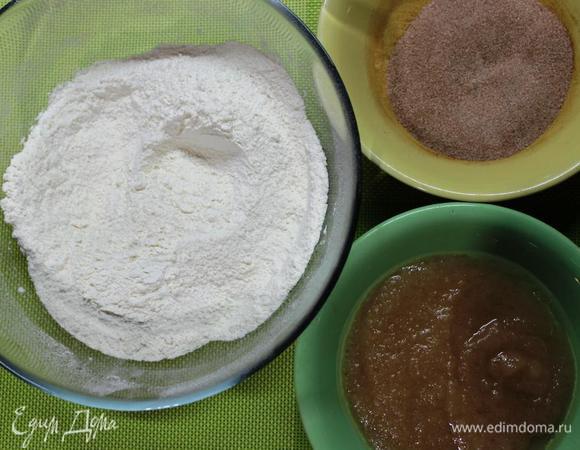 Все просто и быстро. 
Ставим духовку на разогрев до 180 градусов.
В одной миске смешиваем просеянную муку, разрыхлитель, соду, ванилин и сахар. В другой несладкое яблочное пюре, растительное масло и уксус. В третьей корицу с 2 ст. л. сахара.