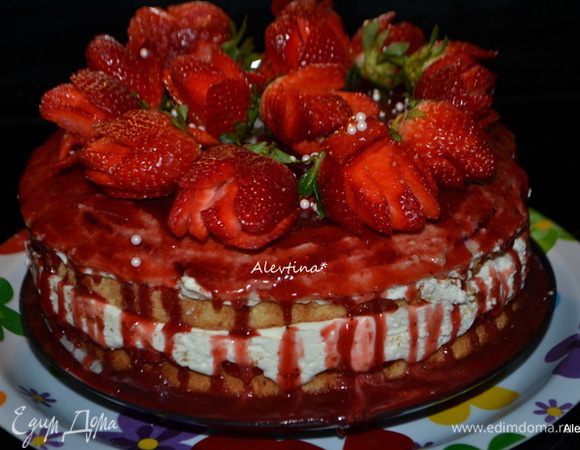 Торт достанем из холодильника, поставим на страховочную широкую тарелку и поливаем теплым клубничным желе со всех сторон, чтобы желе стекал. Выложим приготовленные розочки клубники и вернем в холодильник на некоторое время.