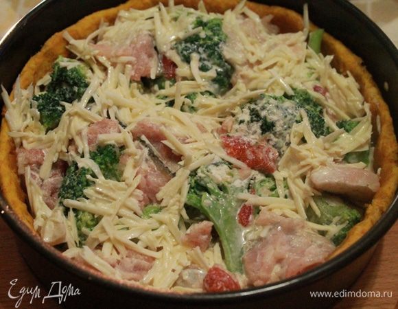 Достать тесто, убрать груз и выложить рыбу и капусту вперемешку. Вылить заливку, равномерно распределяя сыр по начинке. 