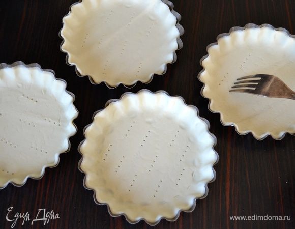 Формочки для тарталеток слегка смазать оливковым маслом и выложить в них тесто. Наколоть вилкой, чтобы тесто не вздулось при выпечке. 