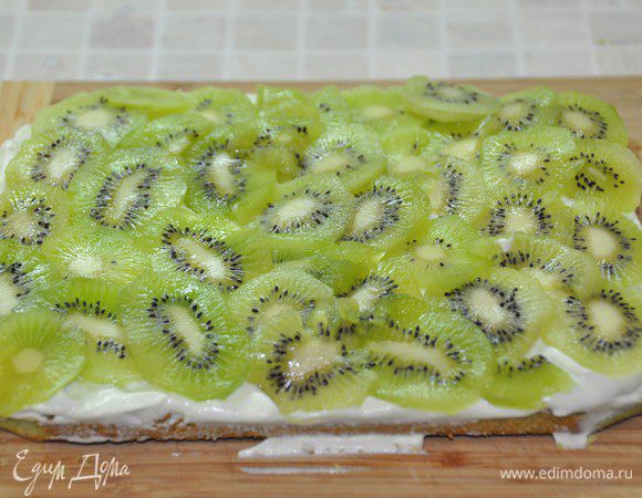 Нижний корж намазать кремом зеленого цвета, уложить пластинки киви.