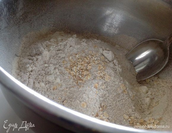 Два вида муки просеять и смешать вместе. Добавить овсяные хлопья, разрыхлитель, сахар и соль. Все хорошо перемешать.