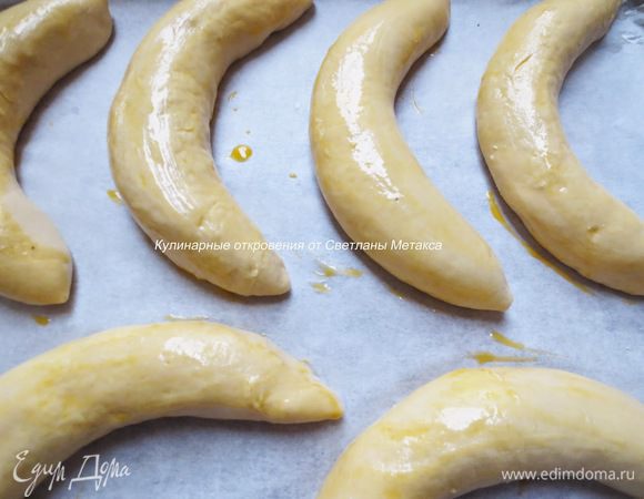 Противень застелить бумагой для выпечки, положить булочки. Взбить яичный желток с водой и смазать поверхность булочек.