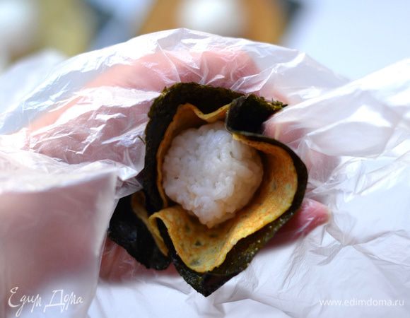 На руку положить целлофан, на него конструкцию с нори. Края нори смазать водой. Зажать в руке, потом скрутить, формируя шарик. Дать полежать минут 5.