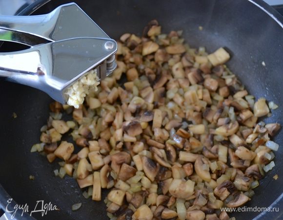 Затем выложить в сковороду нарезанные грибы и выдавить чеснок. Жарить все 2 минуты.
