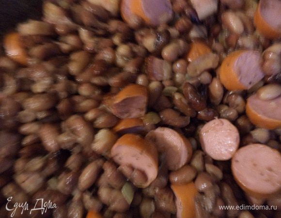 Добавить фасоль, посолить, поперчить, перемешать.
Добавить нарезанные кружками сардельки и порезанную зелень петрушки, перемешать.