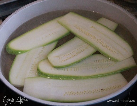 В кастрюлю налейте воду и вскипятите. 
Цукини нарежьте тонкими пластинами и отварите в кипяченой воде 7- 8 минут. Обсушите на бумажном полотенце.