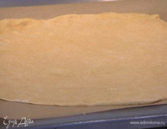 Рабочую поверхность присыпать оставшейся мукой, раскатать из теста большую лепешку, выложить на выстеленный бумагой для выпечки противень и дать тесту немного подойти.