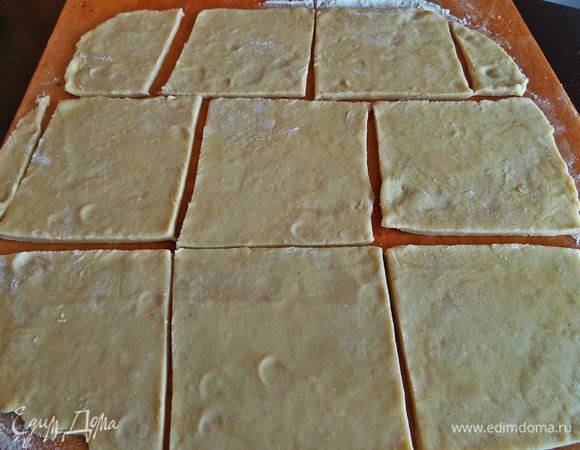 Вынимаем тесто, отрезаем примерно треть (остальное убираем в холодильник) и раскатываем тонко в квадрат или прямоугольник. Нарезать на квадратики. Дополнительную муку я указала для присыпки на доску.
