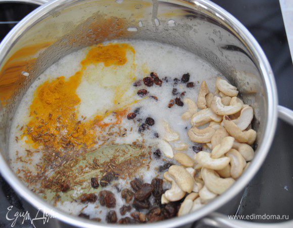 Добавить кокосовое молоко, воду (для тех, кто не соблюдает пост можно добавить куриный бульон), специи, соль, лавровый лист, изюм и орехи. Перемешать. Накрыть крышкой, довести до кипения и убавить нагрев до минимального. Варить в течение примерно 20 минут до готовности. Крышку в период готовки не открывать.
