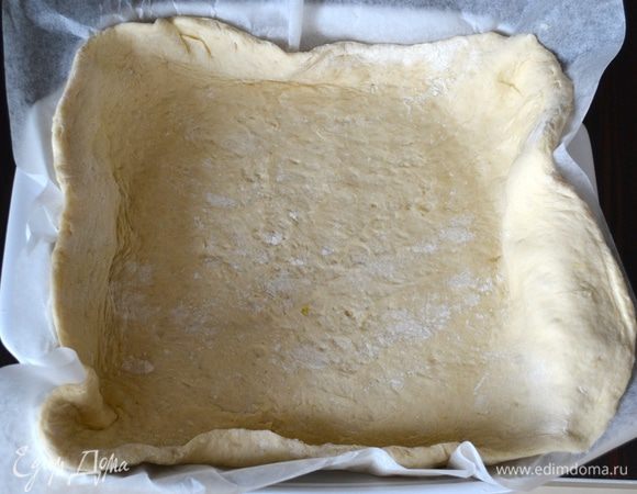 Духовку разогреть до 200°C. Квадратную форму для выпечки (25 см) выложить пекарской бумагой. Готовое тесто перенести на рабочую поверхность. 2/3 части от теста раскатать в пласт около 1 см и выложить в подготовленную форму.