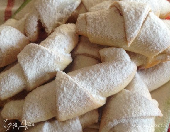 Если Вы используете все тесто (это где-то 2 противня изделий), поделите его на 6 равных частей, если, как я половину, значит на 3. Скатайте шарики, раскатайте один из них, остальные на время уберите в холодильник. Далее стандартная схема изготовления рогаликов: раскатать круг, поделить на 8 частей, положить начинку (в оригинале варенье из лепестков роз, любое другое густое варенье и даже обычный сахар) и скрутить рогалик. На просыпанный мукой противень выложить изделия и отправить в разогретую до 180 градусов духовку, печь до золотистой корочки. Еще теплыми обвалять в сахарной пудре! Есть, когда остынут!