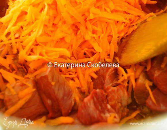 Тем временем помыть, очистить и натереть на крупной терке морковь. К луку выложить мясо, сельдерей, морковь и выдавленный через пресс чеснок. Постоянно помешивая, томить овощи и мясо 3-5 минут.