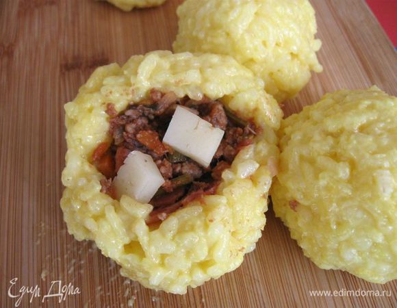 Берем один шарик, кладем на ладонь, пальцем делаем углубление (чем больше поместится начинки у вас, тем лучше, рисовая оболочка при этом не должна страдать). Кладем начинку, добавляем несколько кубиков сыра. Немного сжимаем рукой, прикрывая начинку полностью  рисом. Так же поступаем со всеми остальными шариками риса. 