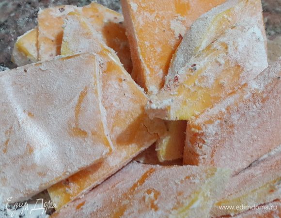 Тыкву нарезаем пластиками толщиной не более 0,5 см. Солим, посыпаем перцем, сушеным базиликом и мукой. Перемешиваем, равномерно распределяя по кусочкам тыквы. Отставляем в сторону на 7-10 минут.