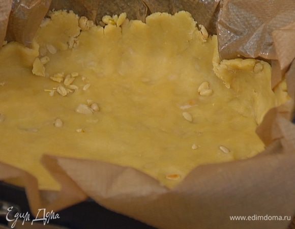 Бумагу для выпечки смазать оставшимся сливочным маслом, выложить в центр тесто, скалкой раскатать его в пласт, превышающий диаметр формы. Уложить бумагу с тестом в разъемную форму и сформировать из теста бортики. Поместить сверху еще один лист бумаги, высыпать на него килограмм гороха или любой крупы и отправить форму в разогретую духовку на 20 минут.