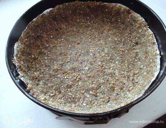 Орехи и семечки измельчить с помощью мясорубки. Изюм также измельчить в мясорубке. Смешать с орехами и семечками, добавить кардамон, предварительно растертый. Добавить немного воды, чтобы масса схватилась. Форму (у меня разъемная, диаметром 20 см) застелить бумагой для выпечки или фольгой. Выложить основу, сделать небольшие бортики. У меня бортики оказались немного выше, чем я хотела. В следующий раз я бы сделала их пониже. И слой "теста" тоже можно делать немного тоньше. Поэтому я все-таки посоветовала бы взять орехов поменьше, грамм 150, а, может, и 100! Готовую основу убрать ненадолго в холодильник.