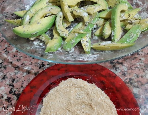 Возвращаемся к авокадо. Аккуратно руками перемешиваем ломтики. Панировочные сухари смешиваем с кунжутными семечками. Обваливаем каждый ломтик в сухарях.