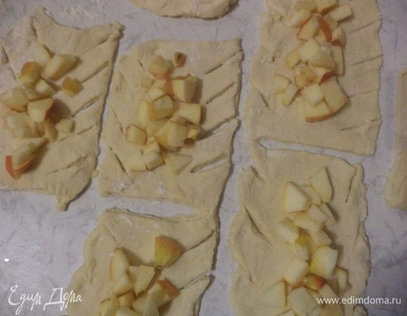 В центр каждого прямоугольника выложить яблоки, посыпать сахаром.
По краям теста с двух сторон сделать диагональные надрезы.
