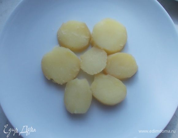 На тарелку выкладываем кольцами порезанный картофель, который мы предварительно сварили в мундире. Поливаем заправкой.