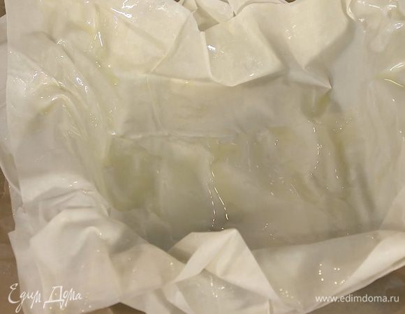 Три листа фило кисточкой смазать оливковым маслом и уложить в форму один на другой смазанной стороной вверх, так чтобы края теста свешивались из формы (последний лист смазать побольше).