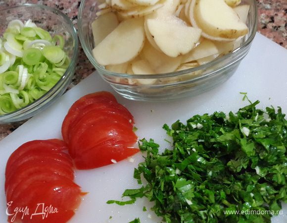 Картофель моем щеткой и режем тоненькими пластиками, лук - кружочками, помидоры полукружочками. 
Петрушку и чеснок мелко рубим и перемешиваем между собой.