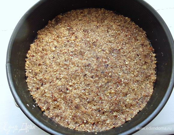 Дно разъемной формы (у меня диаметром 26 см) застелить бумагой для выпечки. Выложить чуть больше половины полученной смеси, равномерно распределить ее и утрамбовать. Убрать ненадолго в холодильник.