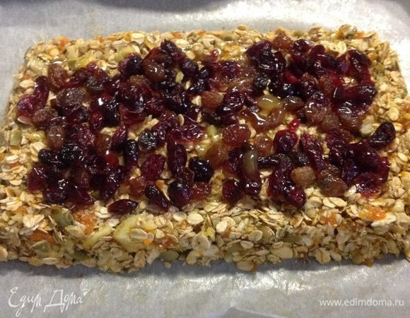 Разогреваем духовку до 200С. На пергамент выкладываем мюсли-массу высотой 2 см, утрамбовываем, формируем прямоугольник, а сверху посыпаем изюмом и вяленой клюквой. Плотно прижимаем, немного вдавливая ягодки и сверху чуть-чуть заливаем мёдом. Ставим в разогретую духовку на 15-20 минут. Смотрим, чтобы не подгорело!