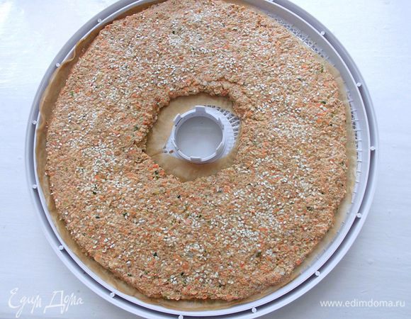 Выложить его на листы дегидратора, предварительно выстеленные бумагой для выпечки. Присыпать сверху кунжутом. Сушить при температуре 40 градусов около 24 часов. Можно также сушить на батарее или в духовке при самой низкой температуре и с приоткрытой дверцей. Когда хлебцы будут уже практически готовыми, но еще мягкими, разрезать их на порционные кусочки (удобнее это делать кухонными ножницами) и уже в таком виде досушить до желаемого состояния. 