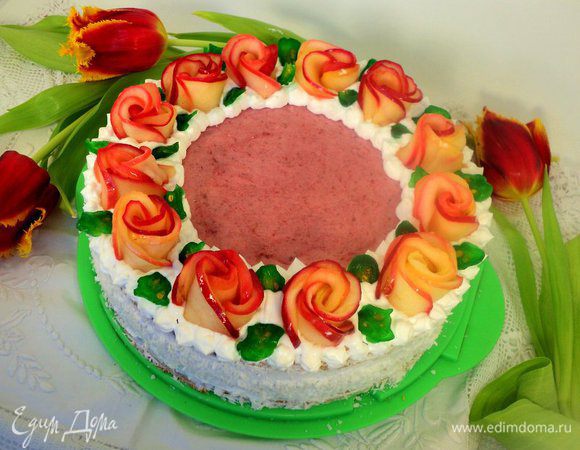 Бока торта смазать взбитыми сливками и обсыпать кокосовой стружкой. Края бисквита декорировать при помощи кулинарного шприца взбитыми сливками и украсить розами из яблок. Листики из порезанного пластинками зеленого кумквата.