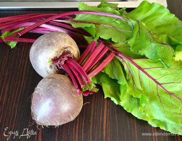 Первым делом включите духовку разогреваться на 190°C. Приступим к подготовке свеклы. Ботву отрезать на расстоянии примерно 2 см от основания корнеплода. Листья промыть и отложить в сторону. Свеклу положить на 5 минут в теплую воду, а затем тщательно вымыть. 