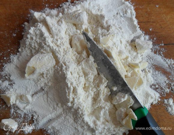 Муку высыпаем на доску, на муку выкладываем холодное сливочное масло и рубим ножом, пока оно не превратится в крошку.